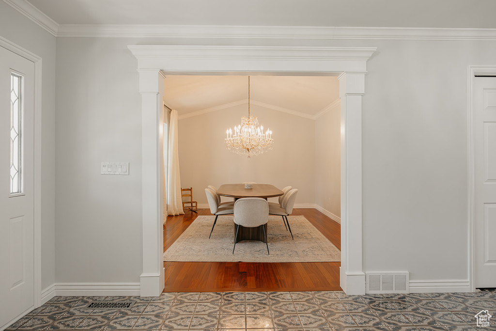 Dining room with an inviting chandelier, wood finished floors, crown molding, visible vents, and baseboards