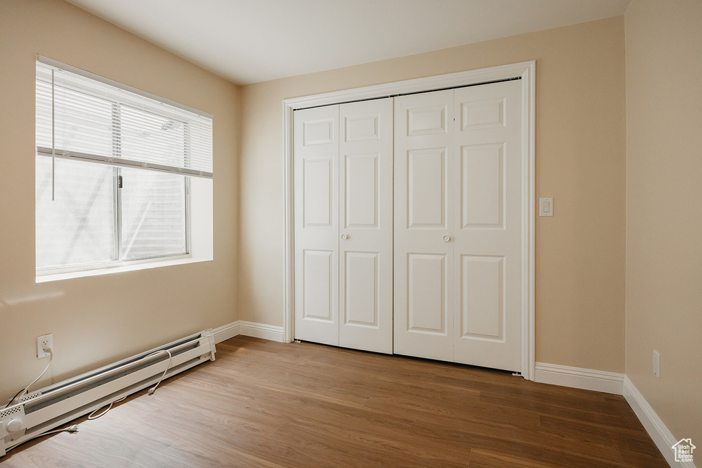 Unfurnished bedroom with baseboards, baseboard heating, and wood finished floors