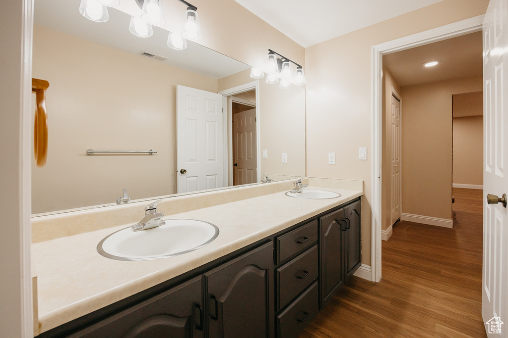 Full bath with double vanity, visible vents, a sink, and wood finished floors
