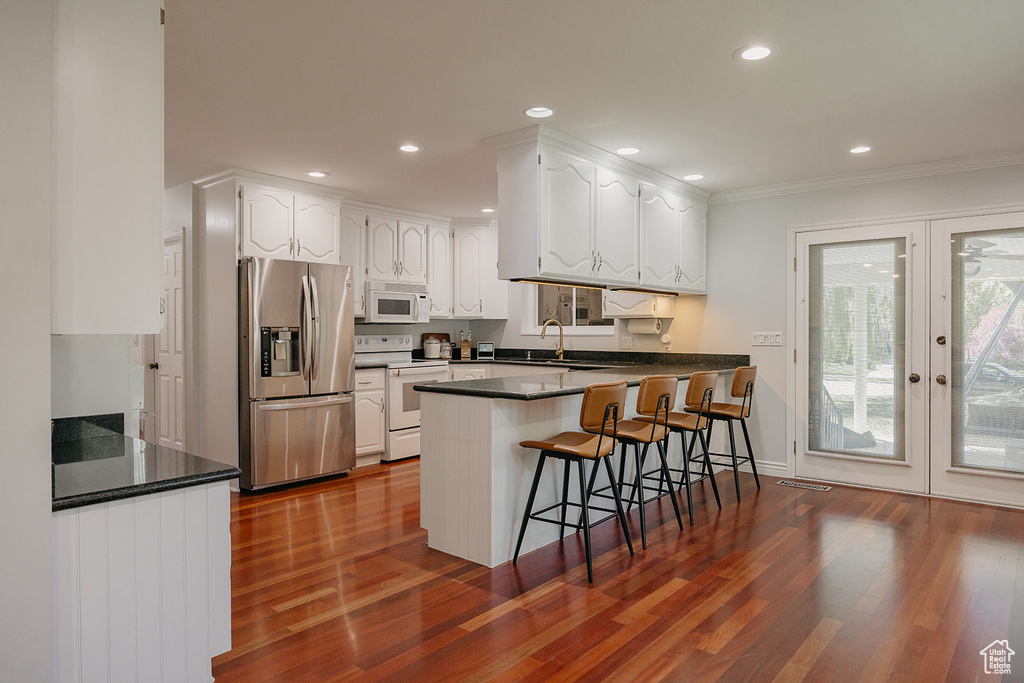 Kitchen featuring a peninsula, white appliances, dark wood-style flooring, white cabinetry, and dark countertops