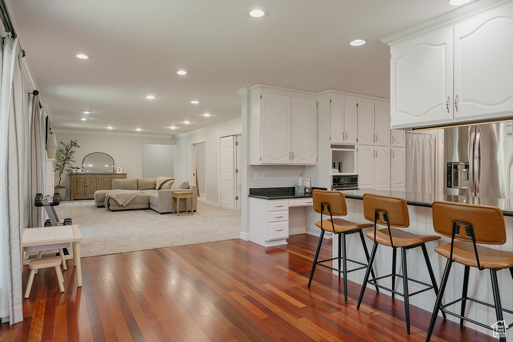 Kitchen featuring a breakfast bar, dark wood finished floors, open floor plan, white cabinets, and dark countertops