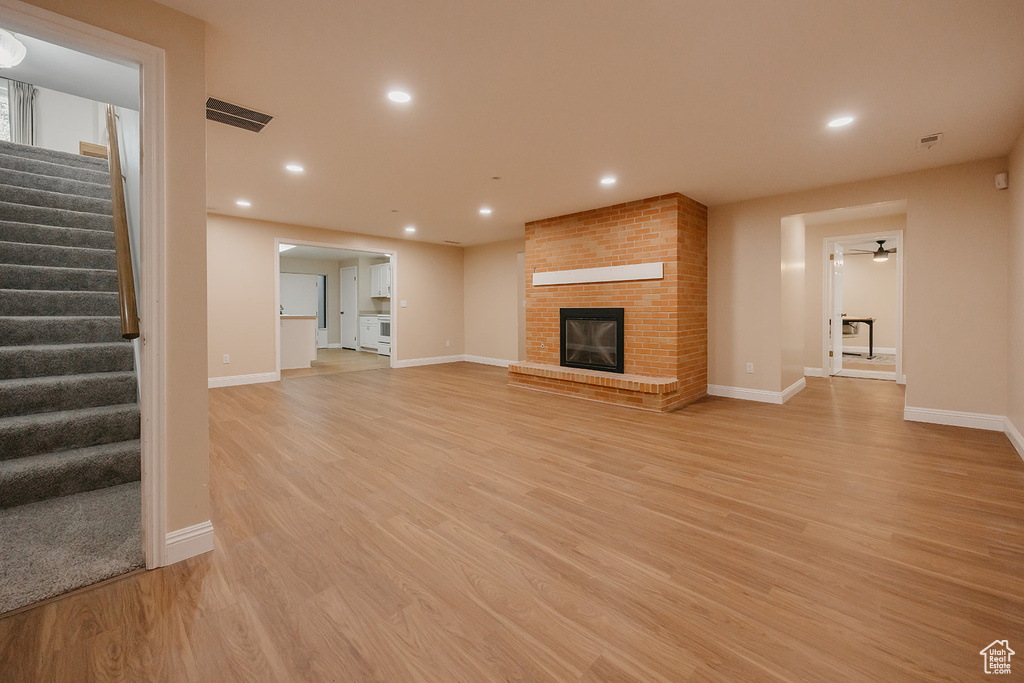 Unfurnished living room with baseboards, visible vents, light wood-style floors, stairway, and a fireplace