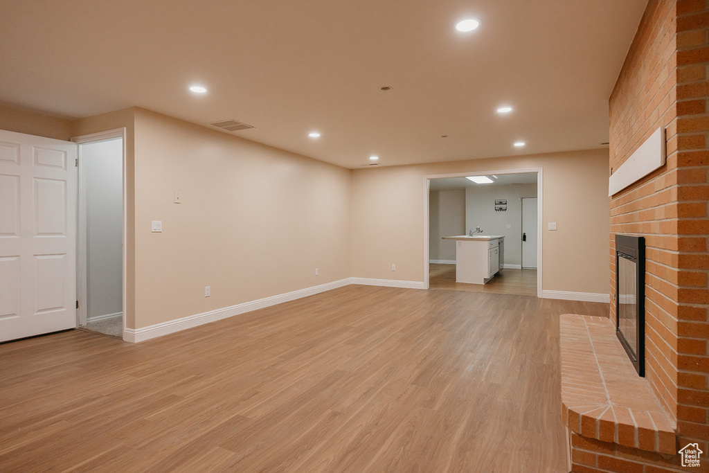 Unfurnished living room featuring light wood-style flooring, a brick fireplace, baseboards, and recessed lighting