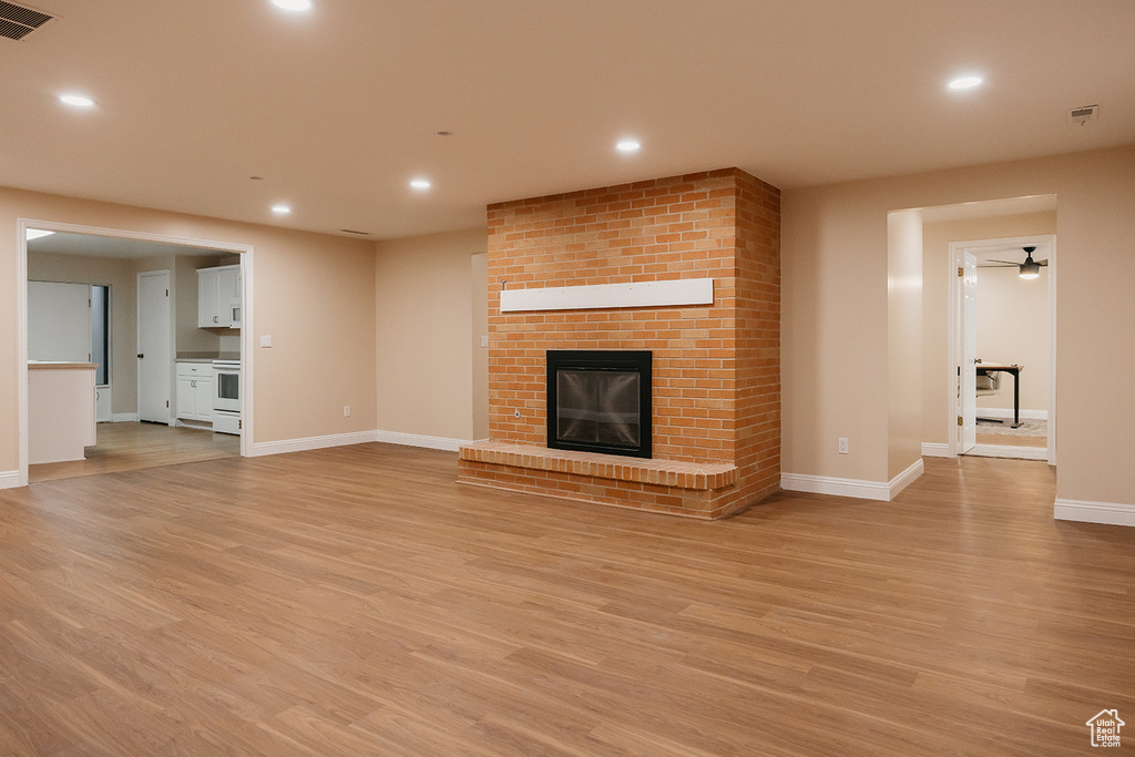 Unfurnished living room with a brick fireplace, visible vents, baseboards, light wood-style floors, and recessed lighting