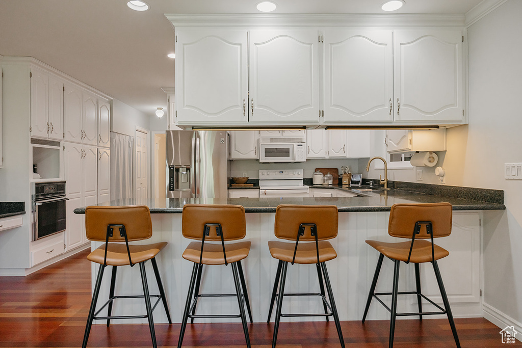 Kitchen featuring a peninsula, a sink, dark countertops, white cabinets, and white appliances