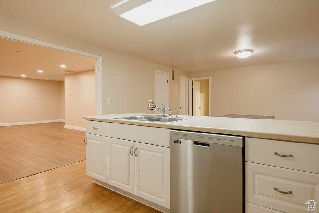 Kitchen with light wood finished floors, dishwasher, white cabinetry, and a sink