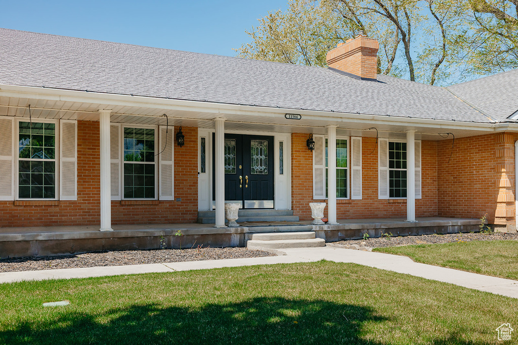 Property entrance featuring a chimney, a lawn, a shingled roof, a porch, and brick siding