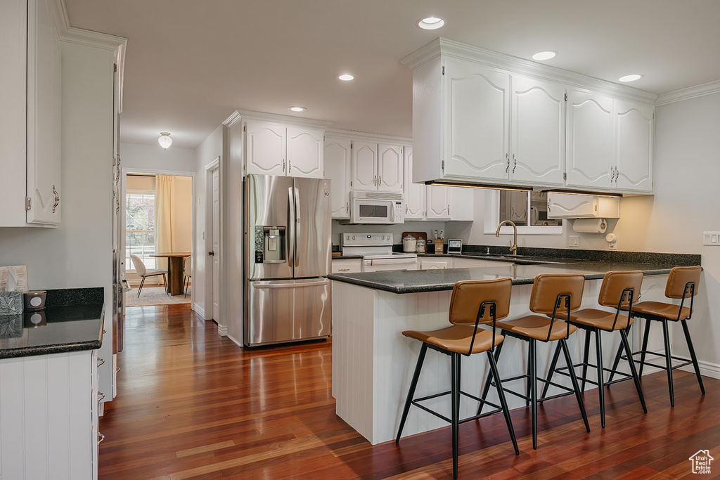 Kitchen featuring white appliances, dark wood finished floors, a sink, white cabinetry, and a peninsula