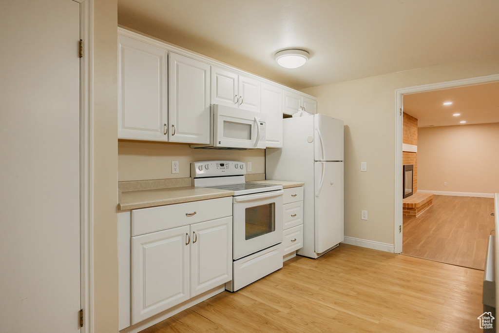 Kitchen featuring white appliances, light wood-type flooring, white cabinetry, a brick fireplace, and light countertops