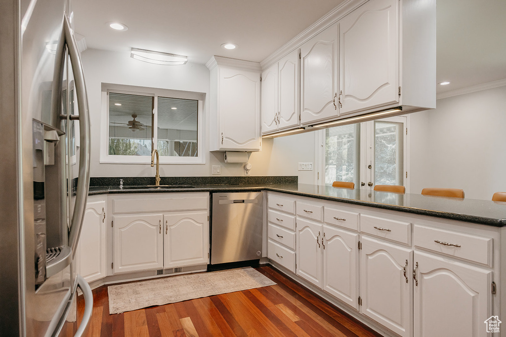 Kitchen with a sink, a peninsula, dark wood-type flooring, white cabinetry, and appliances with stainless steel finishes