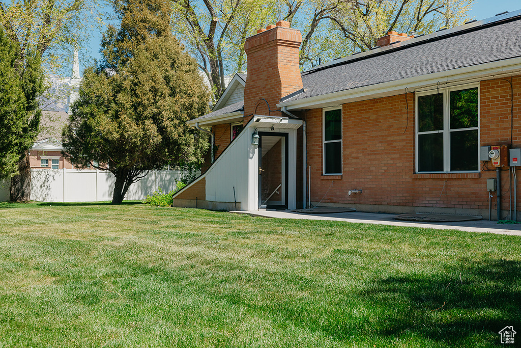 Rear view of property featuring a chimney, brick siding, fence, and a lawn