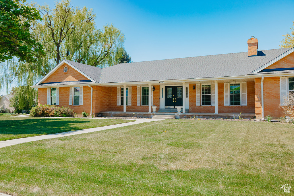 Ranch-style home featuring covered porch, a chimney, a front lawn, and brick siding