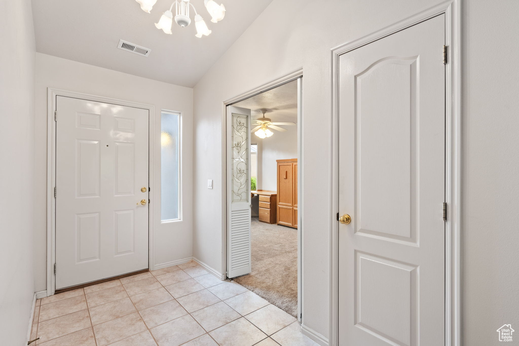 Foyer with a chandelier, light tile patterned floors, vaulted ceiling, baseboards, and light carpet