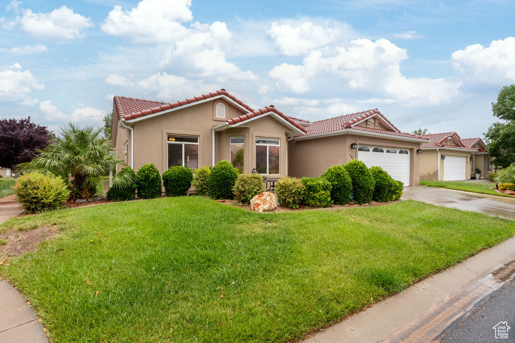 Mediterranean / spanish-style house featuring stucco siding, an attached garage, a tile roof, and a front yard