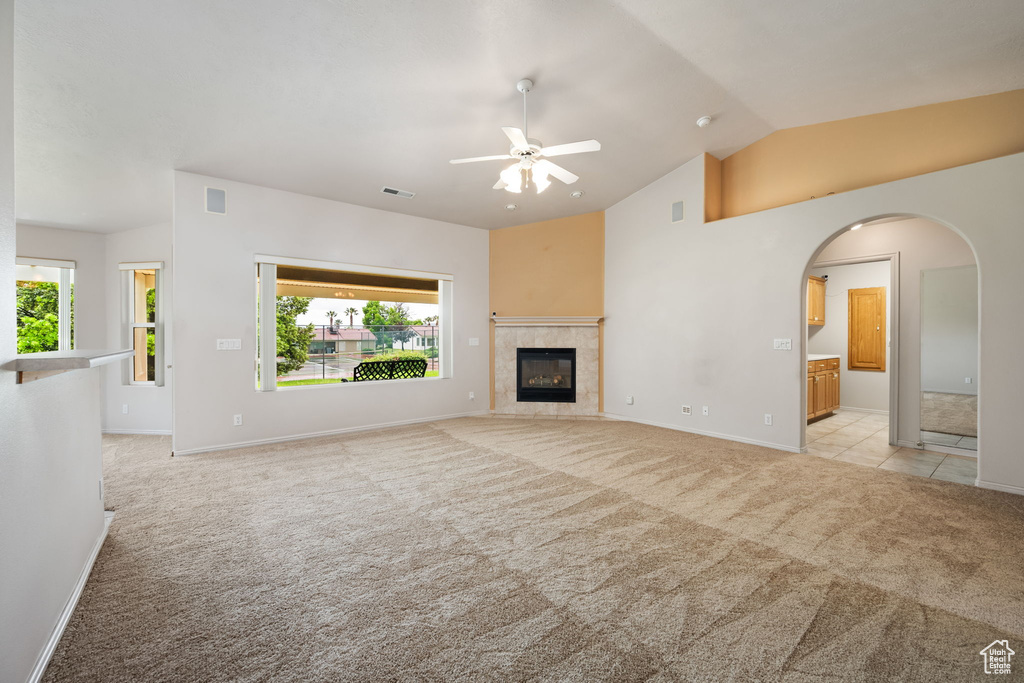 Unfurnished living room with light colored carpet, a ceiling fan, healthy amount of natural light, a fireplace, and high vaulted ceiling