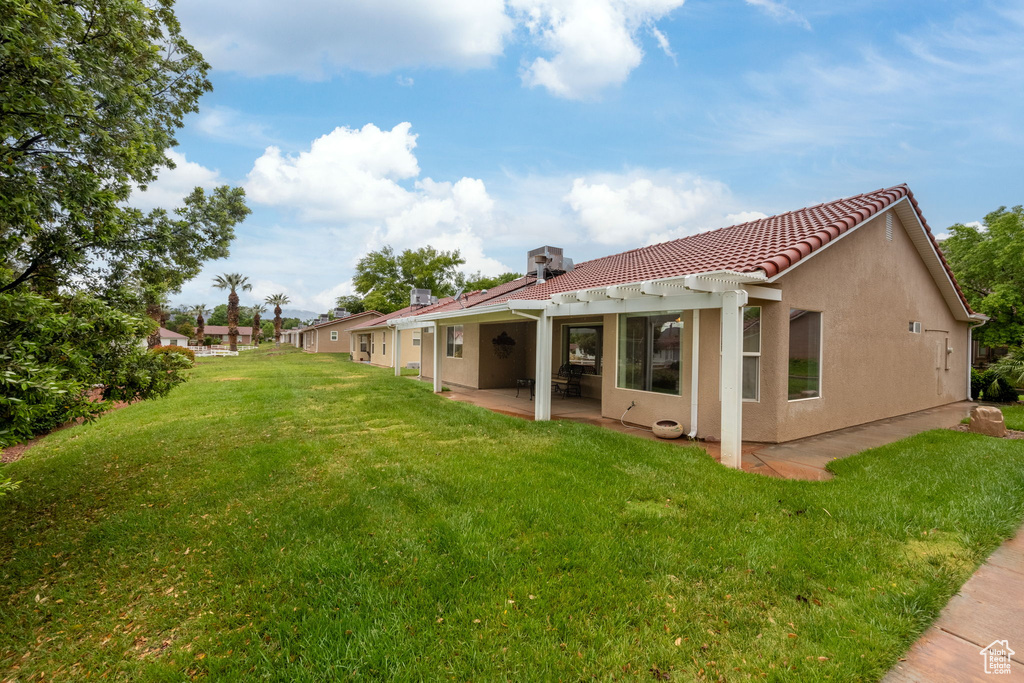 Back of house with a tile roof, a lawn, a patio area, and stucco siding