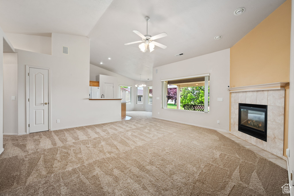 Unfurnished living room with carpet floors, a tiled fireplace, ceiling fan, baseboards, and high vaulted ceiling