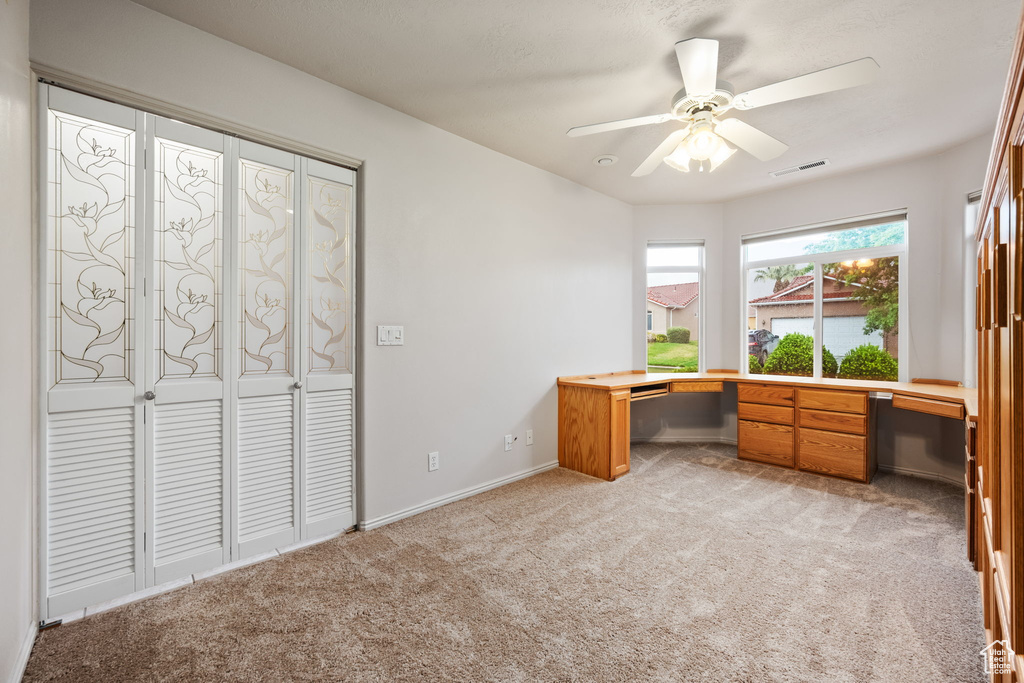 Unfurnished office featuring light colored carpet, a ceiling fan, and baseboards