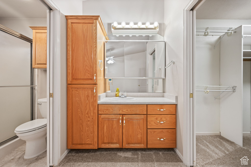 Full bath featuring toilet, vanity, a shower with door, baseboards, and a spacious closet