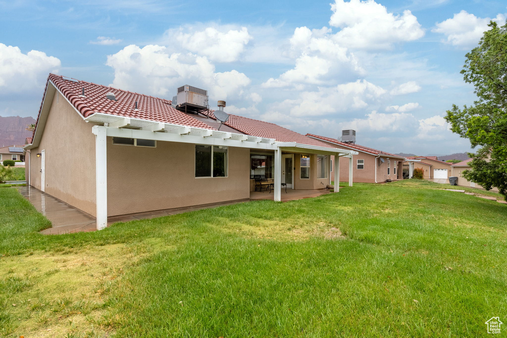 Rear view of property featuring a tile roof, a yard, stucco siding, a patio, and a chimney
