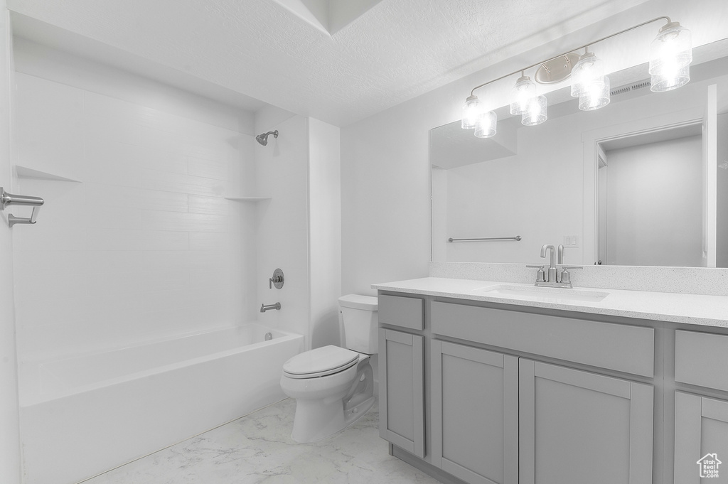 Bathroom with marble look tiles, toilet, vanity, bathtub / shower combination, and a textured ceiling