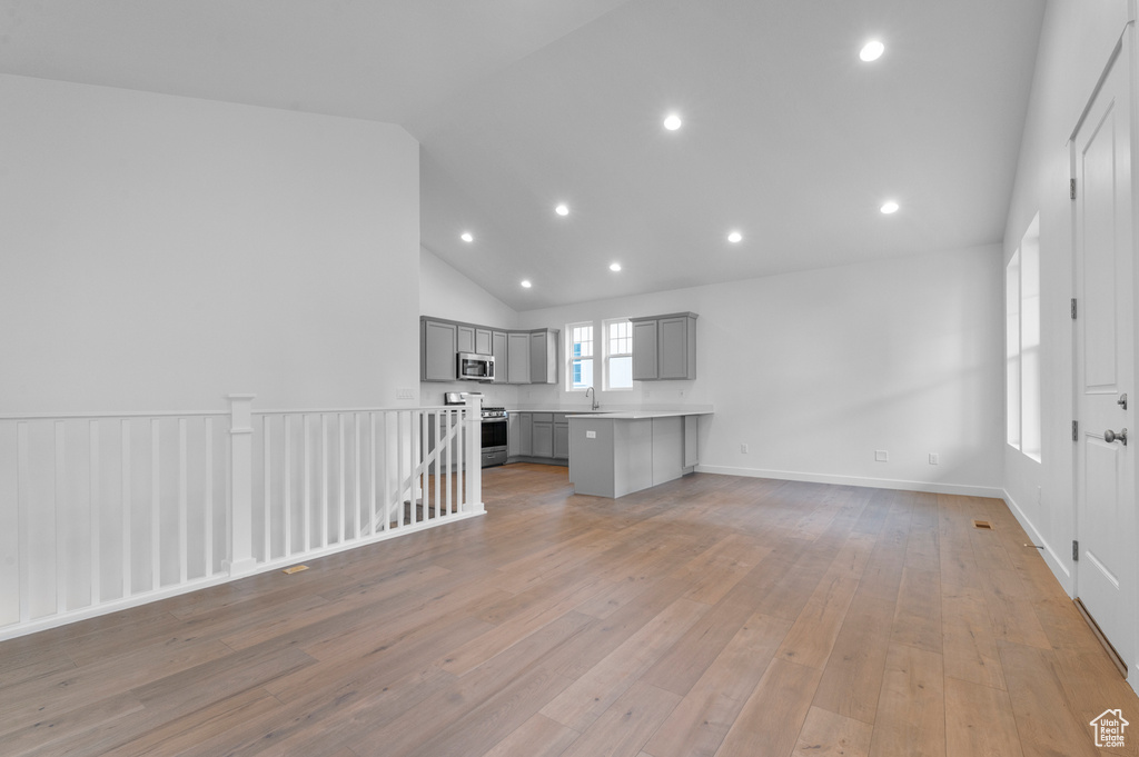 Unfurnished living room with lofted ceiling, light wood-style floors, recessed lighting, and a sink