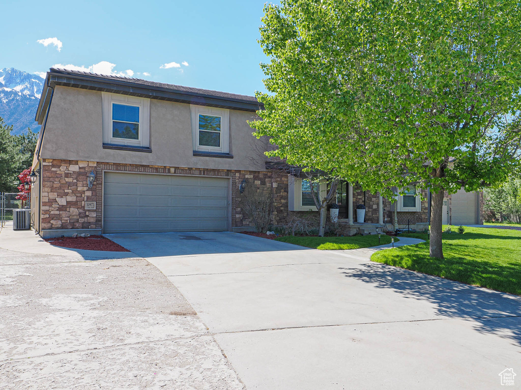 View of front of property with a garage, stucco siding, cooling unit, concrete driveway, and stone siding