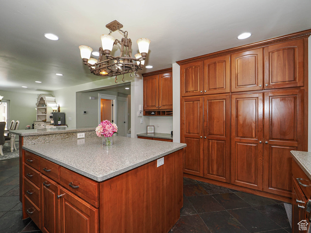 Kitchen featuring a chandelier, a kitchen island, recessed lighting, light countertops, and dark stone finish floors