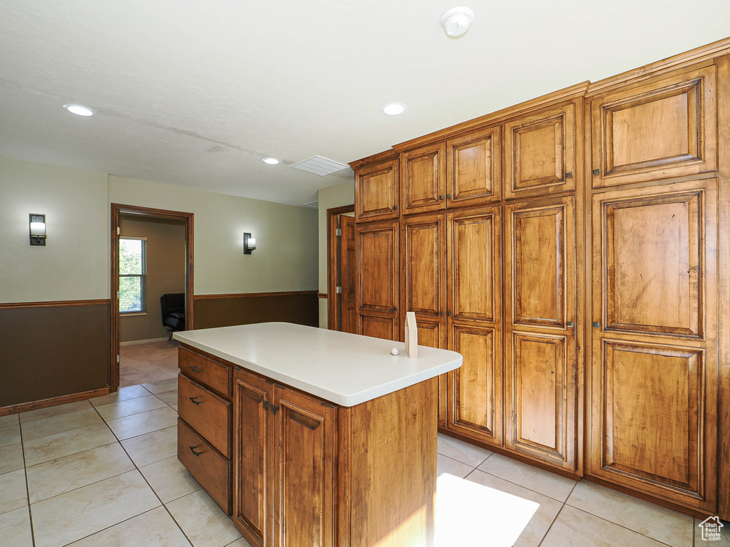 Kitchen featuring brown cabinets, light tile patterned flooring, a center island, recessed lighting, and light countertops