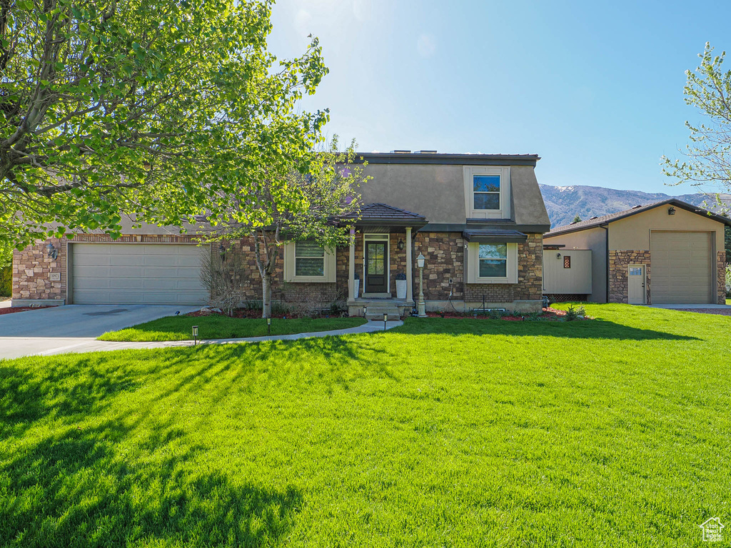 View of front of property featuring stucco siding, a front lawn, driveway, an attached garage, and stone siding