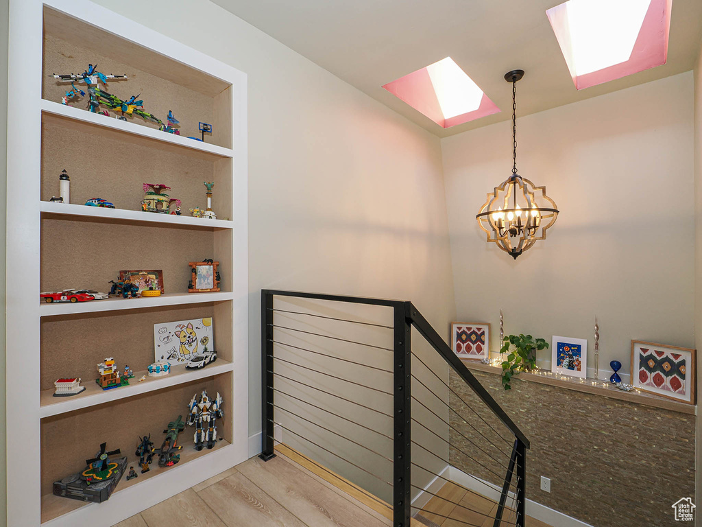 Stairway with a skylight, a chandelier, wood finished floors, and built in shelves