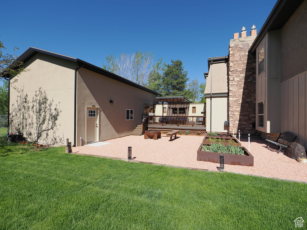 Back of house with a wooden deck, stucco siding, a patio, and a lawn