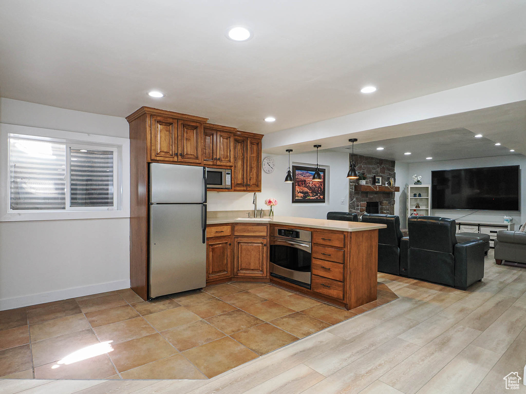 Kitchen with appliances with stainless steel finishes, a peninsula, brown cabinetry, a sink, and open floor plan
