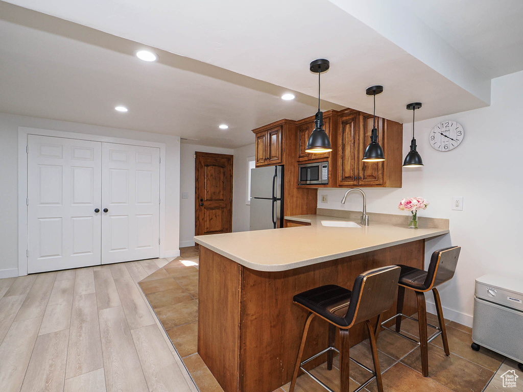 Kitchen featuring stainless steel microwave, freestanding refrigerator, a sink, brown cabinetry, and light countertops
