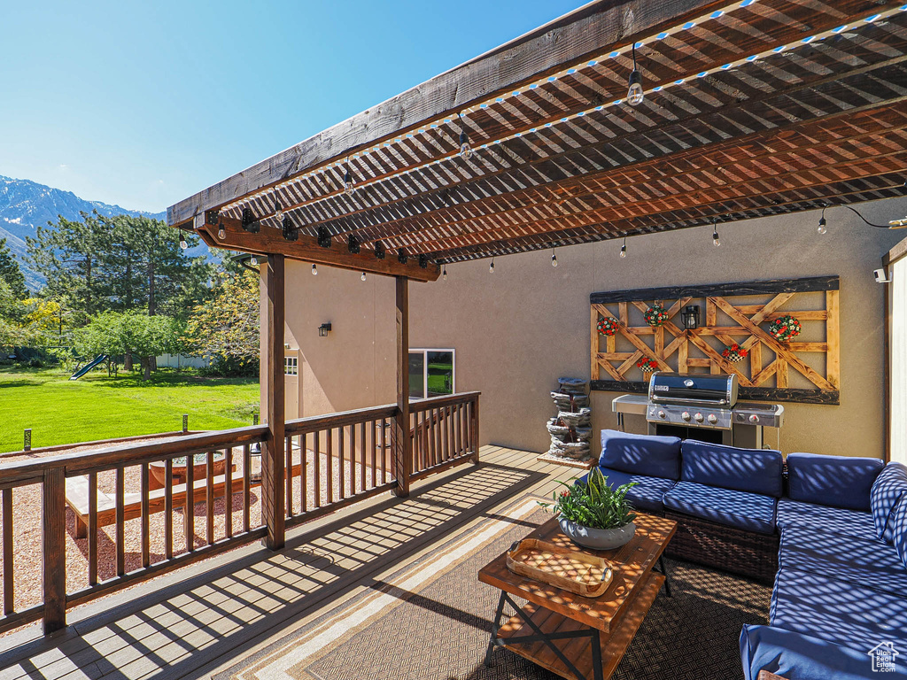Wooden deck featuring area for grilling, an outdoor hangout area, a playground, a lawn, and a mountain view