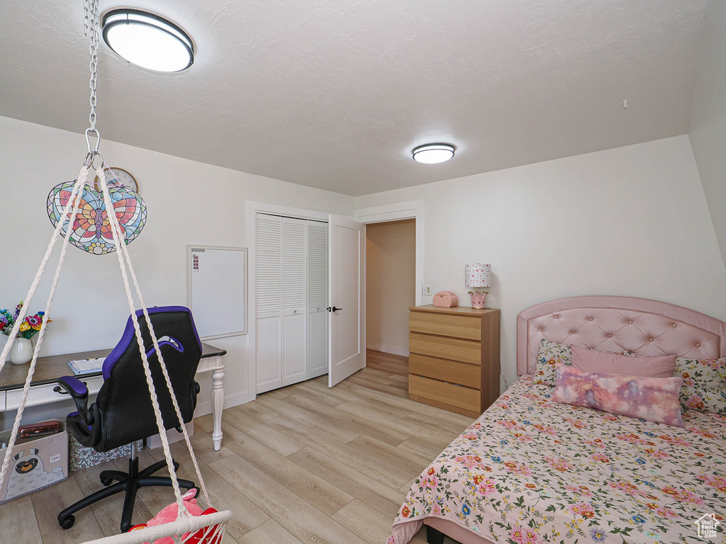 Bedroom featuring light wood finished floors, a closet, an office area, and a textured ceiling