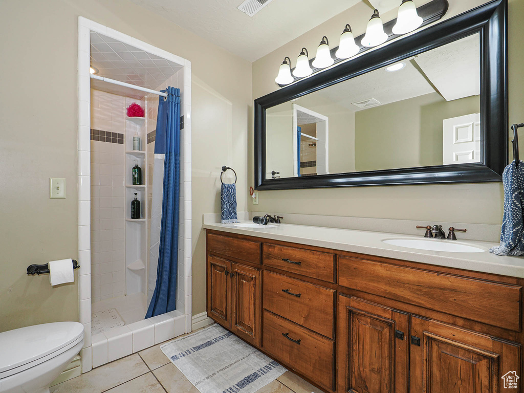 Bathroom featuring tile patterned flooring, a shower stall, toilet, and double vanity