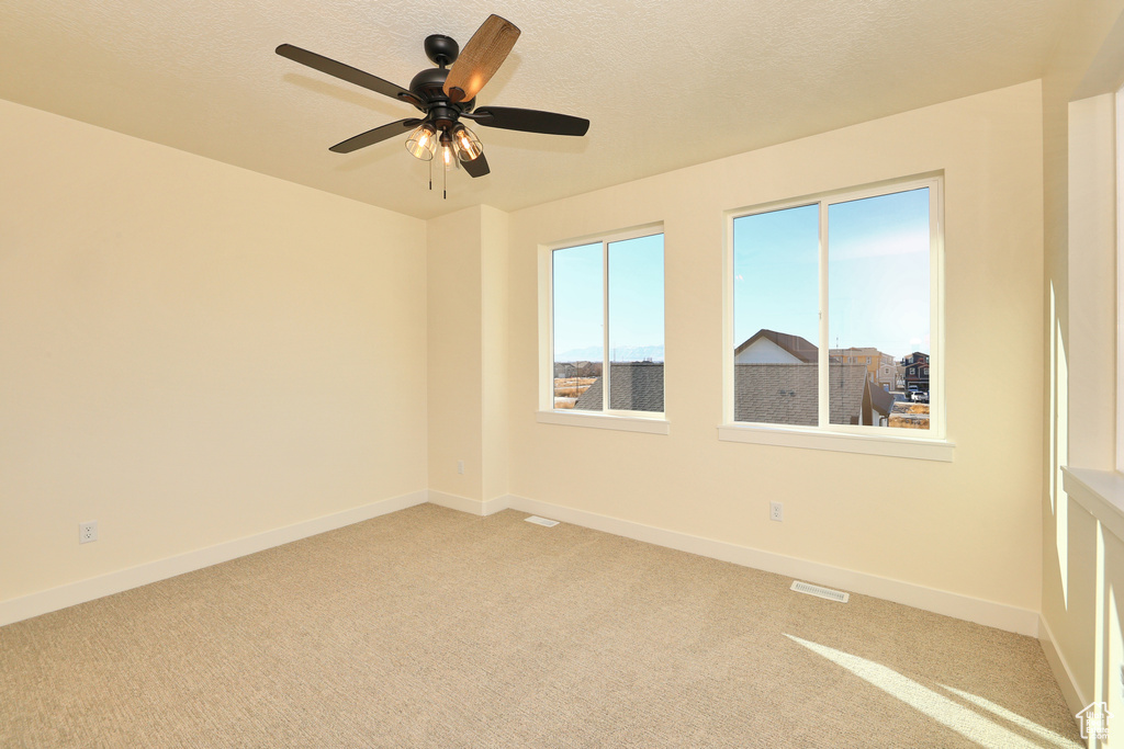 Spare room with light colored carpet, baseboards, a ceiling fan, and a textured ceiling