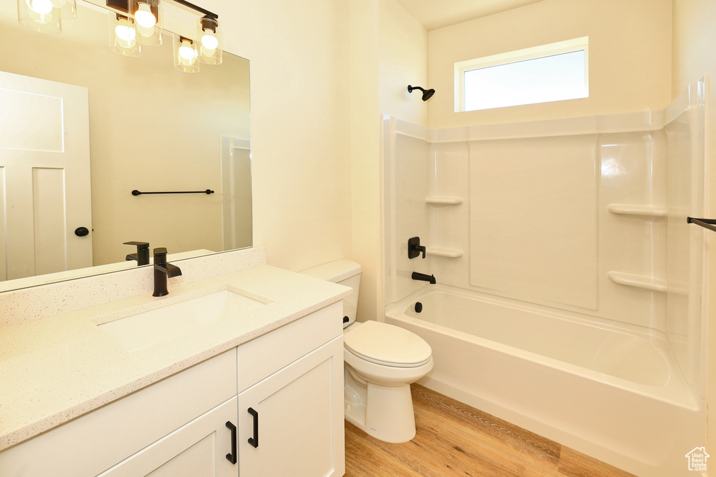 Bathroom with wood finished floors, toilet, vanity, and shower / bath combination