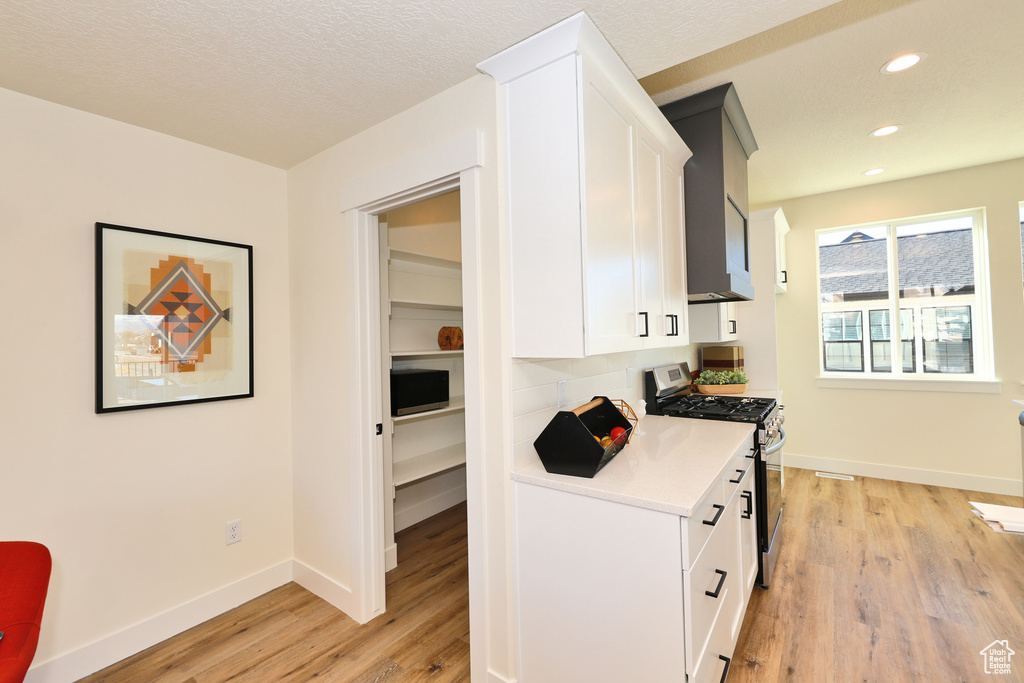 Kitchen with stainless steel range with gas cooktop, white cabinets, light wood-style flooring, light countertops, and baseboards