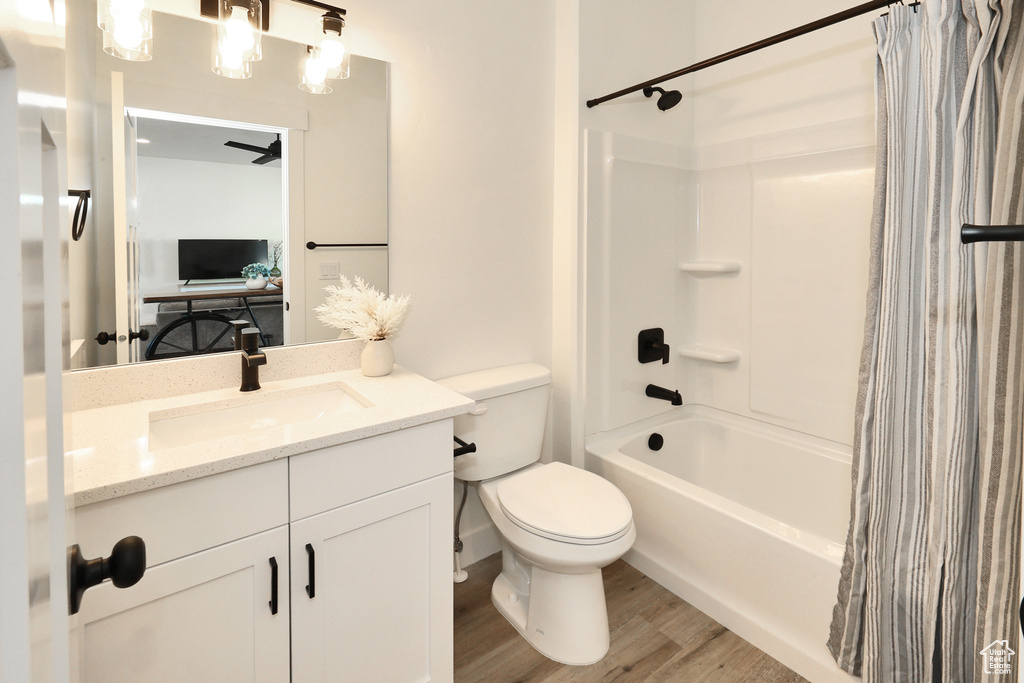 Full bathroom with wood finished floors, toilet, shower / bathtub combination with curtain, and vanity