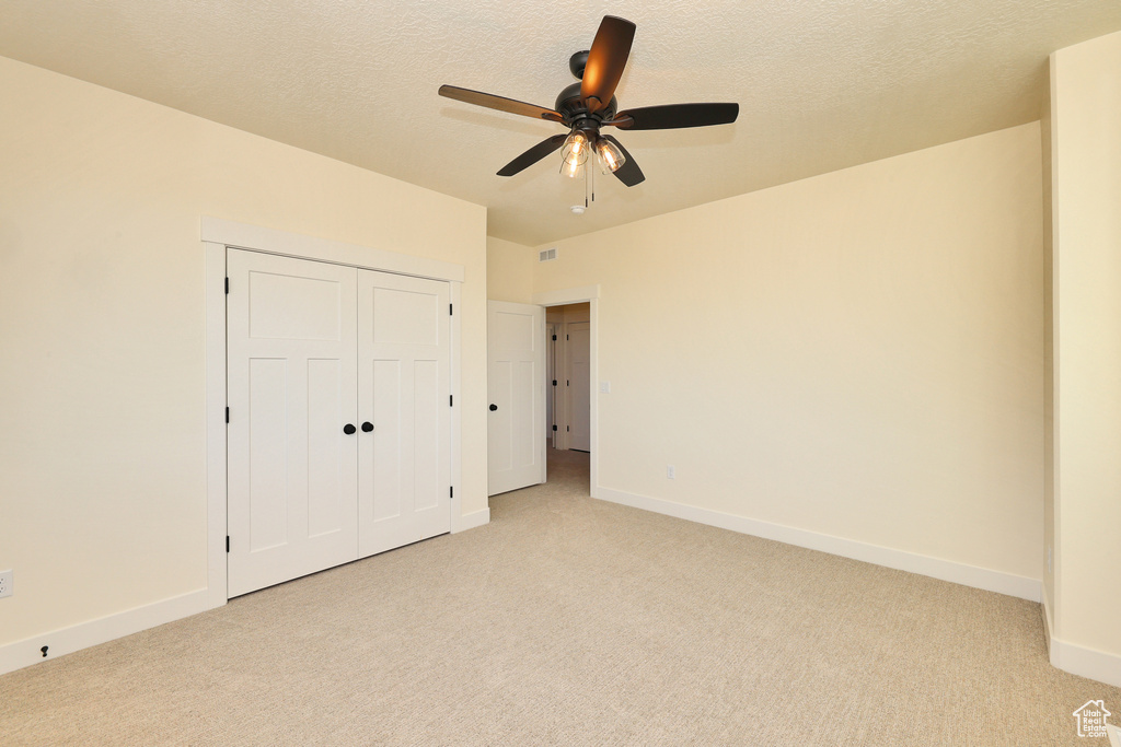 Unfurnished bedroom with light colored carpet, baseboards, a closet, and a textured ceiling