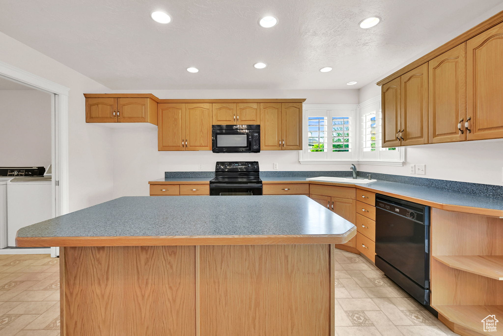 Kitchen with black appliances, washer and dryer, a sink, recessed lighting, and a kitchen island