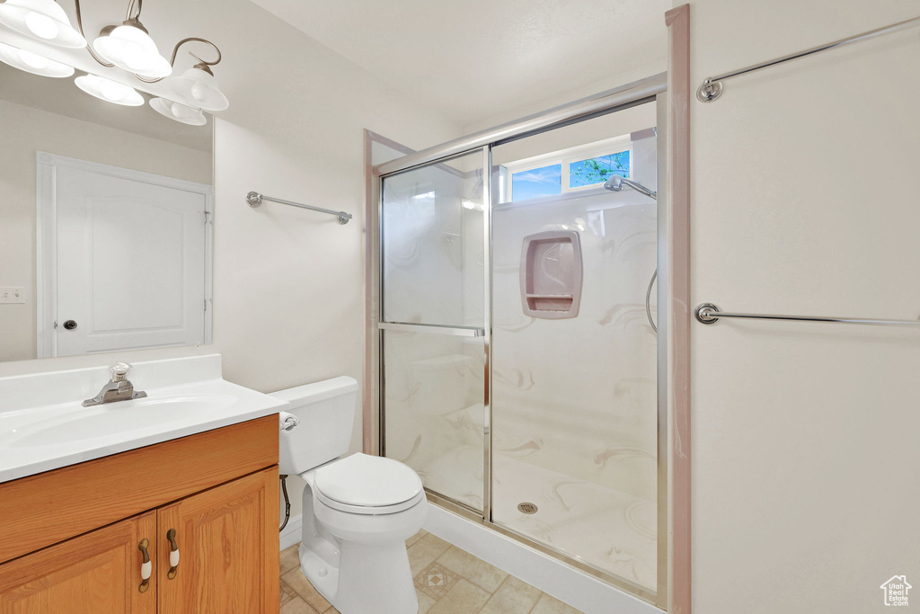 Bathroom featuring a stall shower, toilet, vanity, and a chandelier