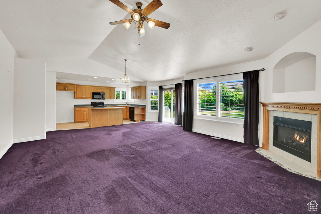 Unfurnished living room with carpet, a tile fireplace, lofted ceiling, ceiling fan, and baseboards