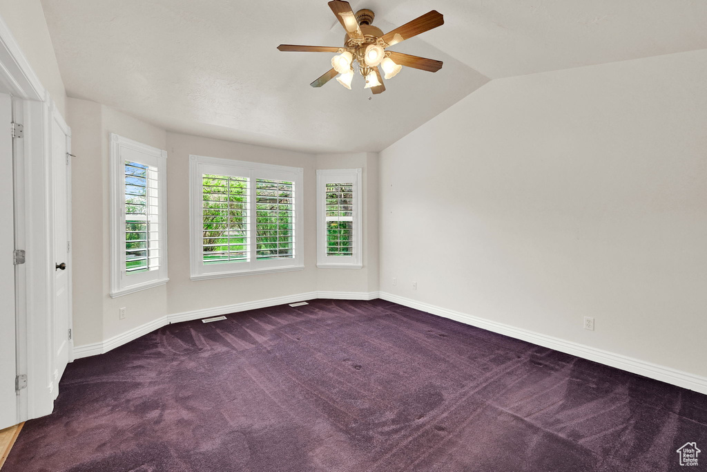 Carpeted spare room featuring ceiling fan, baseboards, and vaulted ceiling