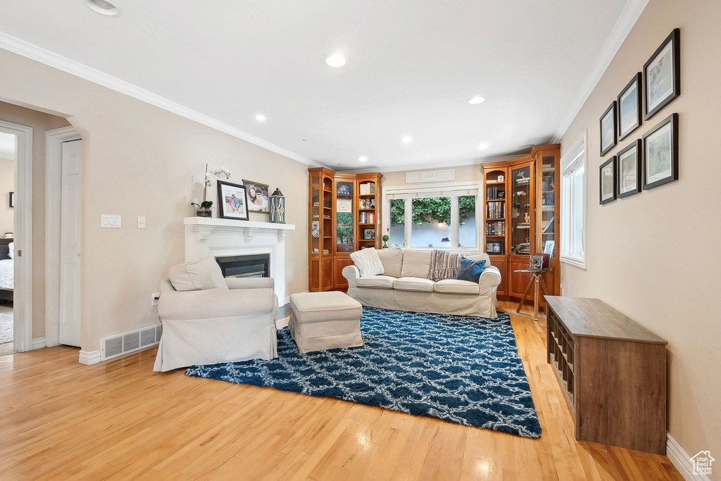 Living area featuring light wood-style flooring, ornamental molding, a glass covered fireplace, baseboards, and recessed lighting
