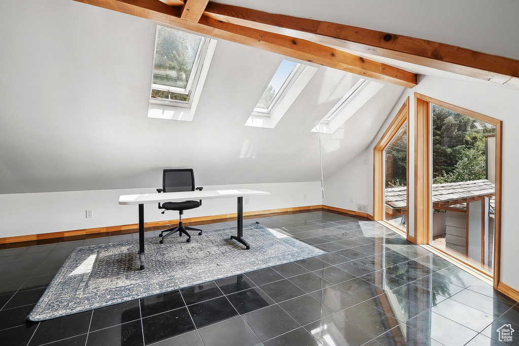 Unfurnished office featuring a skylight, dark tile patterned flooring, and baseboards
