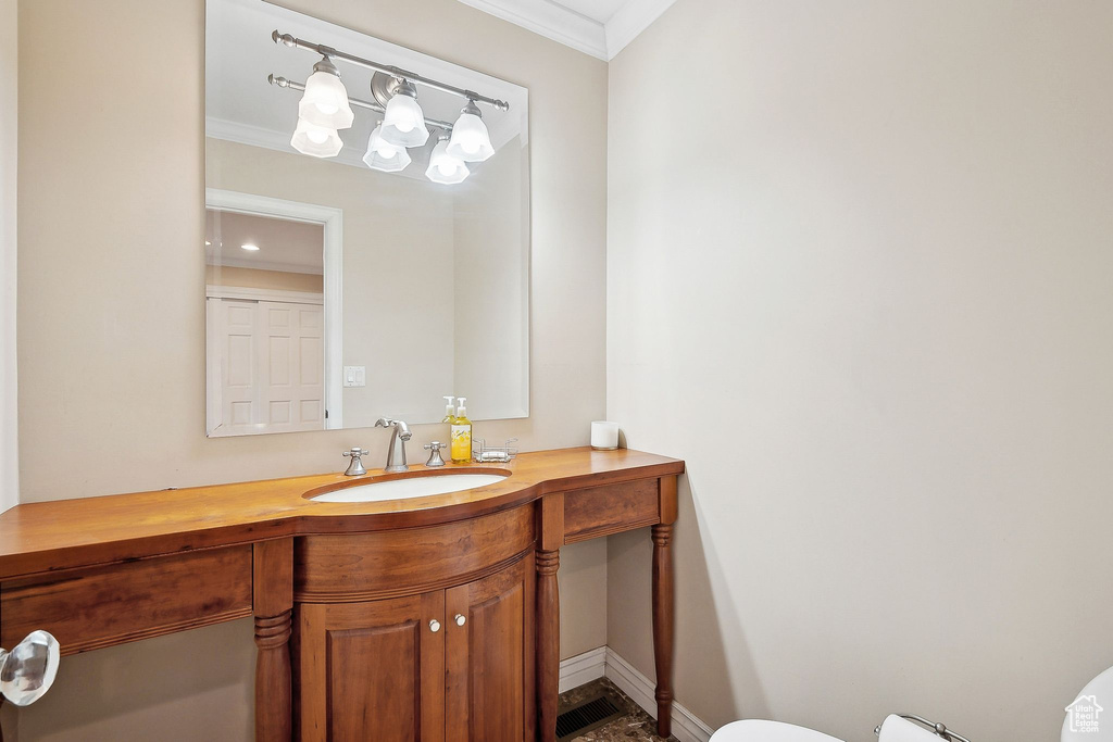 Half bathroom featuring ornamental molding, vanity, toilet, and baseboards