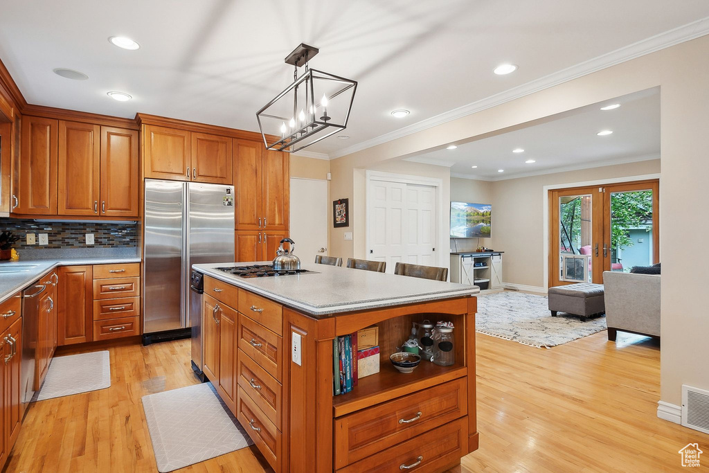Kitchen featuring stainless steel appliances, light wood-style floors, brown cabinetry, crown molding, and a kitchen island